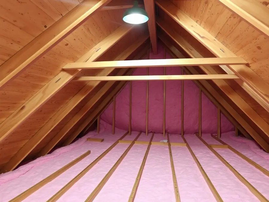 Unfinished attic with wood rafters and roof sheathing overhead, pink insulation between the joists
